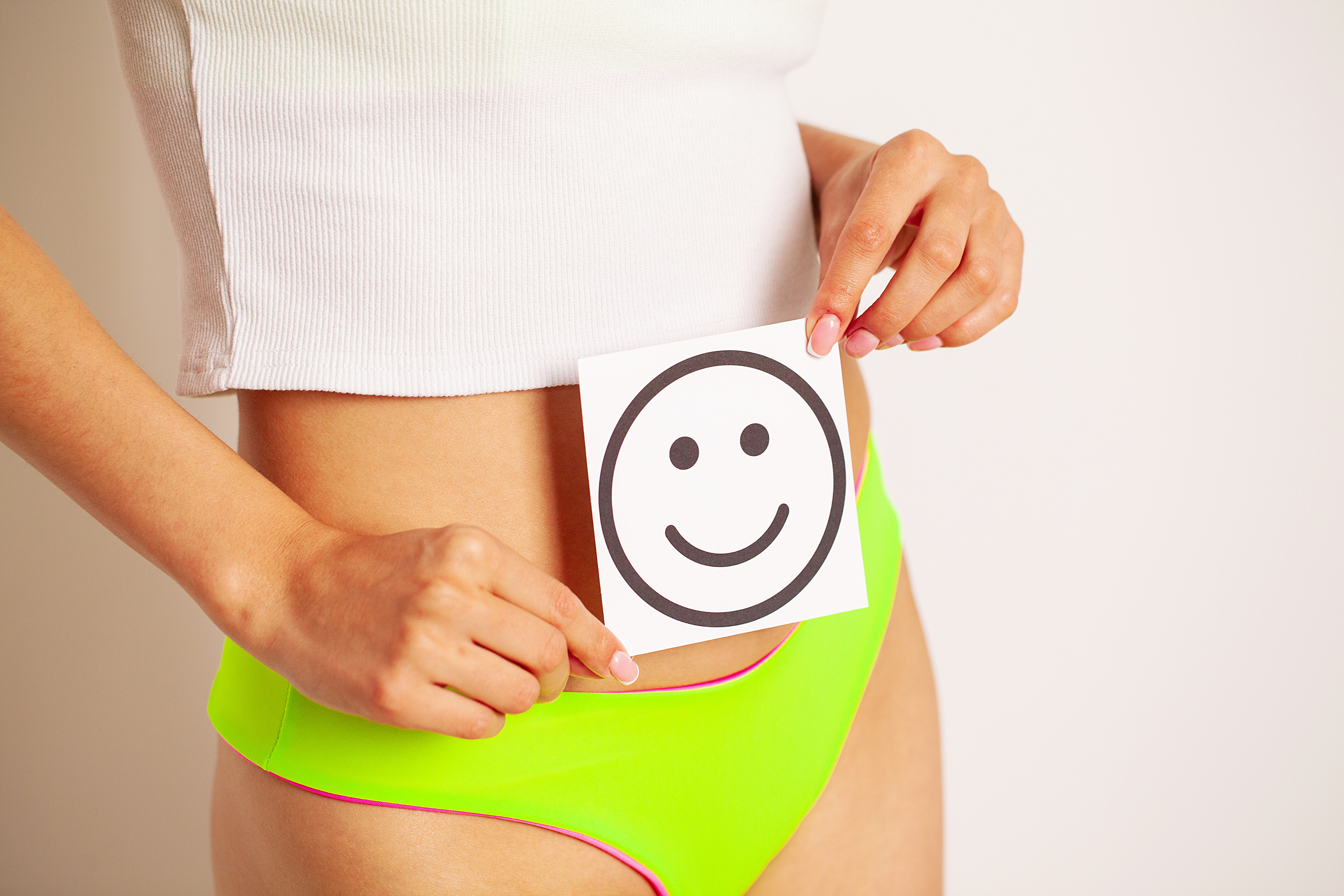 Women stomach health and good digestion concepts, closeup of healthy female with beautiful fit slim body holding white card with happy smiley face in hands